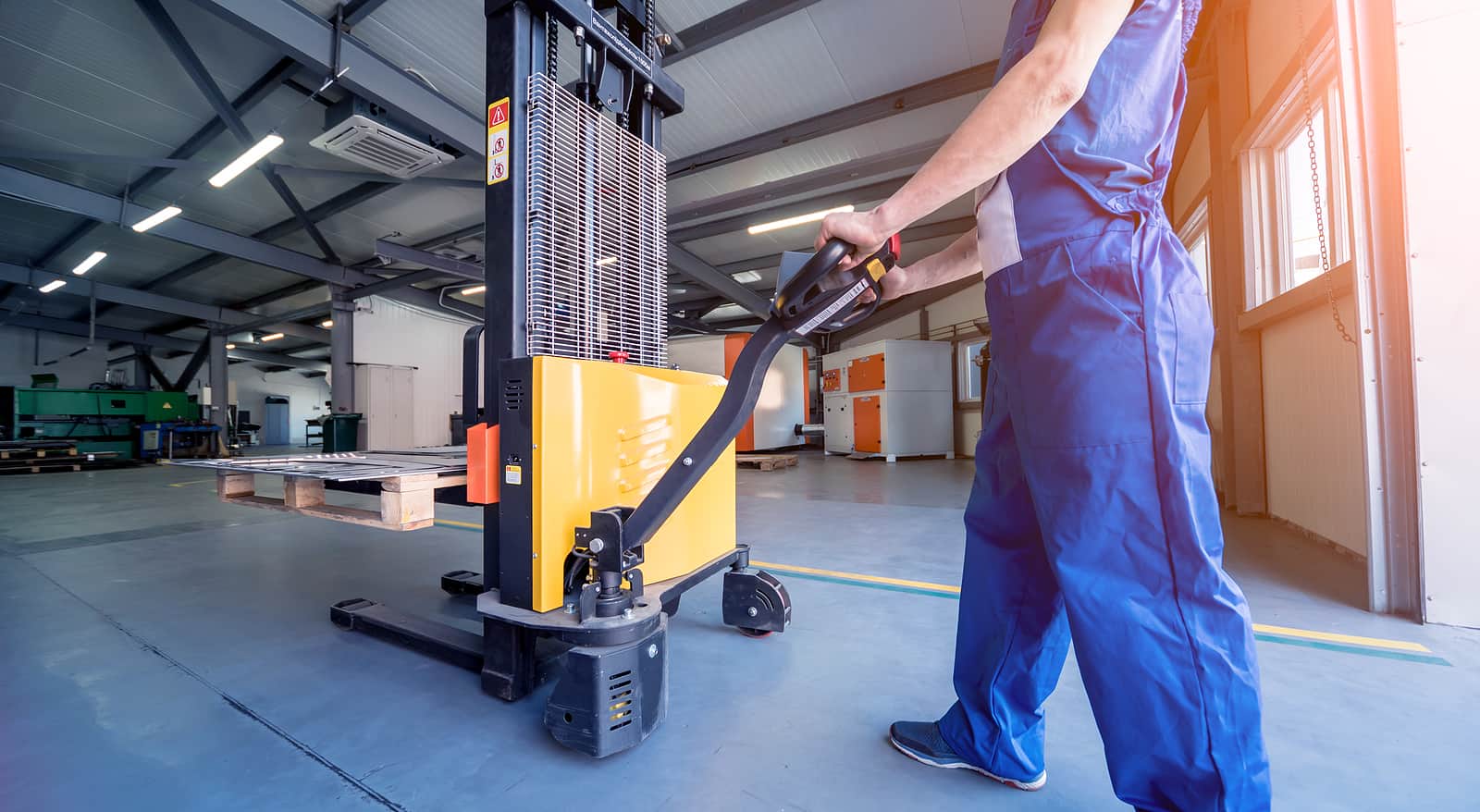 A Worker In A Warehouse Uses A Hand Pallet Truck